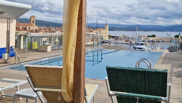 Blick von einem Loungebett auf den Pool und im Hintergrund der Hafen und das Meer. Blick von einem Loungebett auf den Pool und im Hintergrund der Hafen und das Meer.