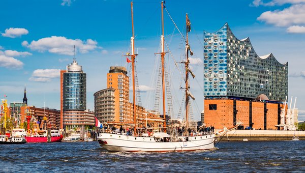 Blick vom Wasser aus auf die Hamburger Elbphilharmonie. Davor ist ein Dreimaster mit eingezogenen Segeln
