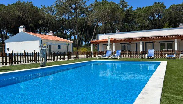 Blick auf den Pool mit Poollift umgeben von ein paar Liegestühlen und im Hintergrund zwei Bungalows und Bäume Blick auf den Pool mit Poollift umgeben von ein paar Liegestühlen und im Hintergrund zwei Bungalows und Bäume