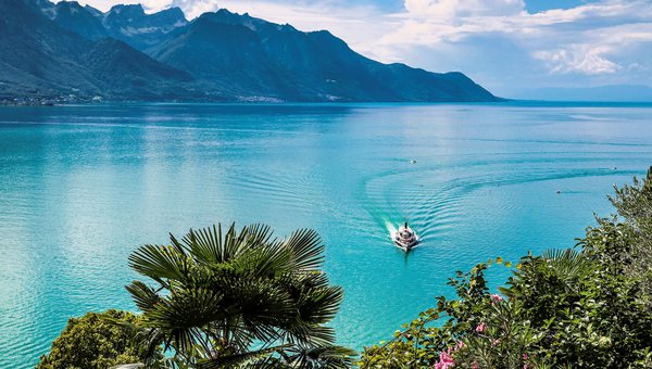 Ein Dampfschiff fährt auf dem Genfersee zum nächsten Hafen. Im Hintergrund sind die Berge.