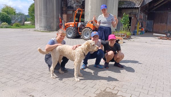 Vier Jugendliche stehen vor einem Bauernhof mit einem grossen Hund.