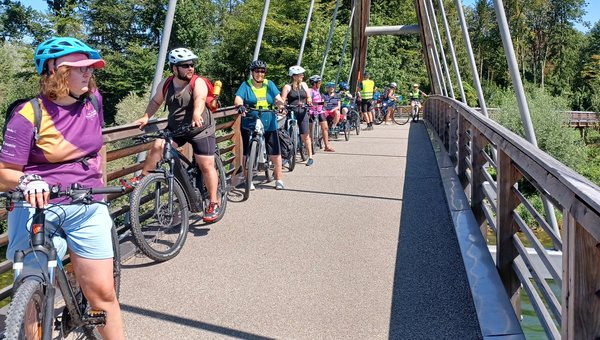 Eine Gruppe Velofahrer*innen geniessen den Blick auf einer Brücke über den Rhein.