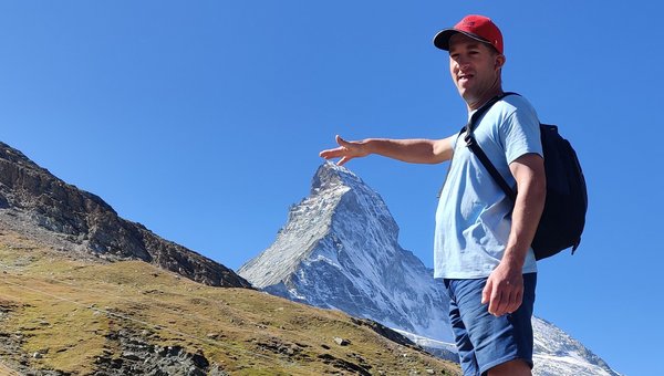 Ein Wanderer berührt durch optische Täuschung die Bergspitze im Hintergrund.