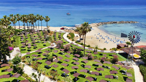 Blick auf den gepflegten Sonnenliegenbereich vom Hotel, umgeben von bunten Blumen und Palmen, direkt am Meer mit Sandstrand