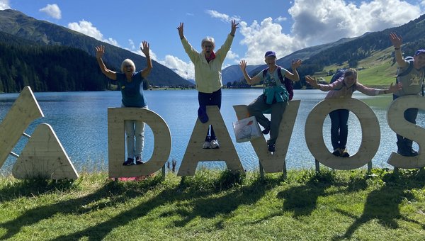Fünf Personen posieren beim Davos-Logo aus Holz vor dem Davosersee.