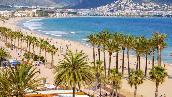 Blick auf den wunderschönen langen Sandstrand mit Palmen in Rosas