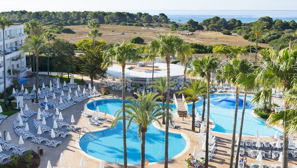 Eine schöne Hotelanlage mit grossem Pool in der Mitte, im Hintergrund sieht man Palmen und das Meer.