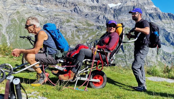 Drei Wandersleute machen vor einer beeindruckenden Bergkulisse eine Pause.