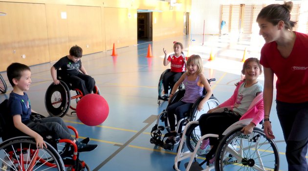 Eine Gruppe Kinder im Rollstuhl spielen in einer Turnhalle