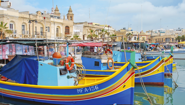 Im Vordergrund bunte Fischerboote im Hafen mit historischen Gebäude im Hintergrund.